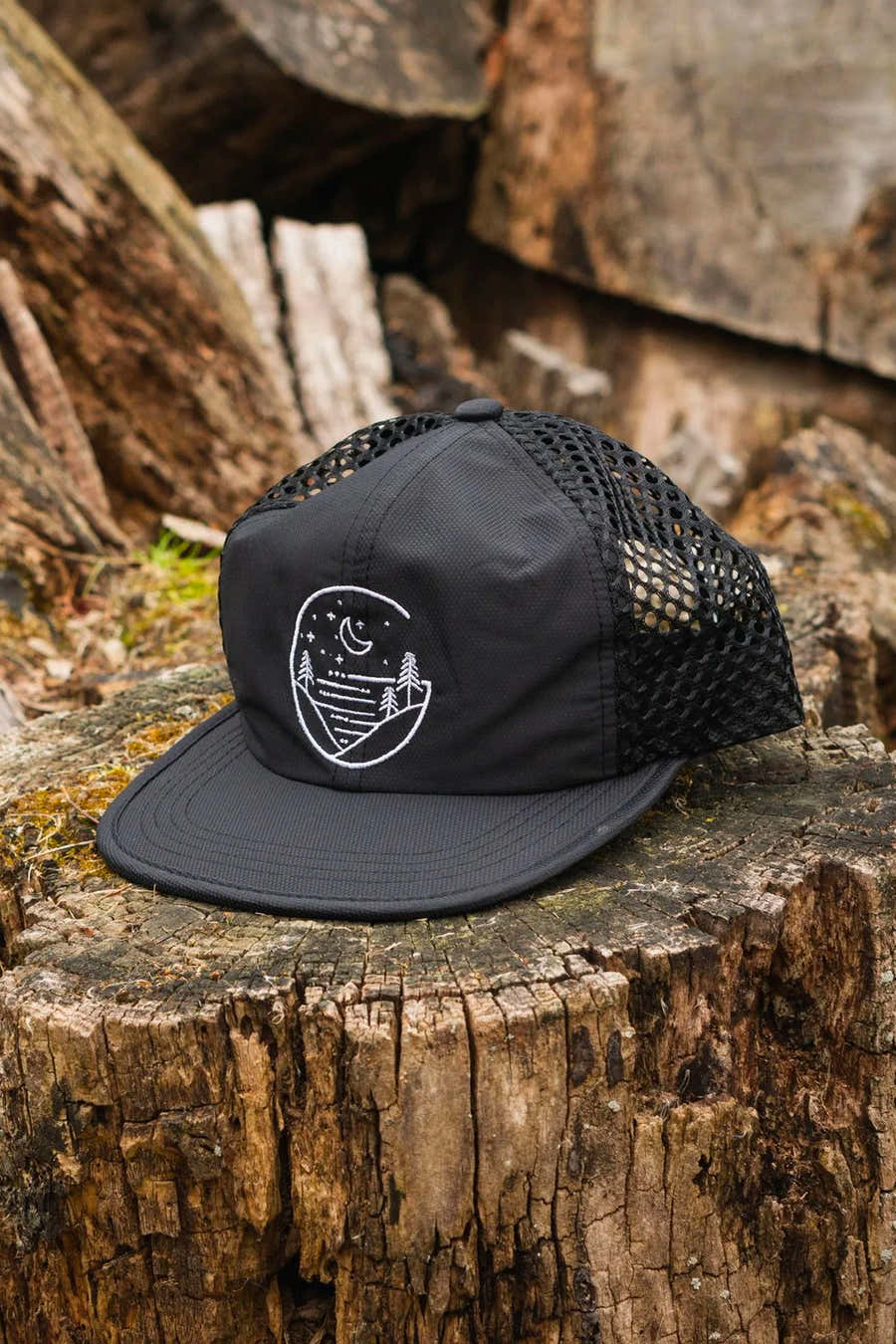 Black Glacial Gear Foldable Trail Hat with mesh sides resting on a tree stump