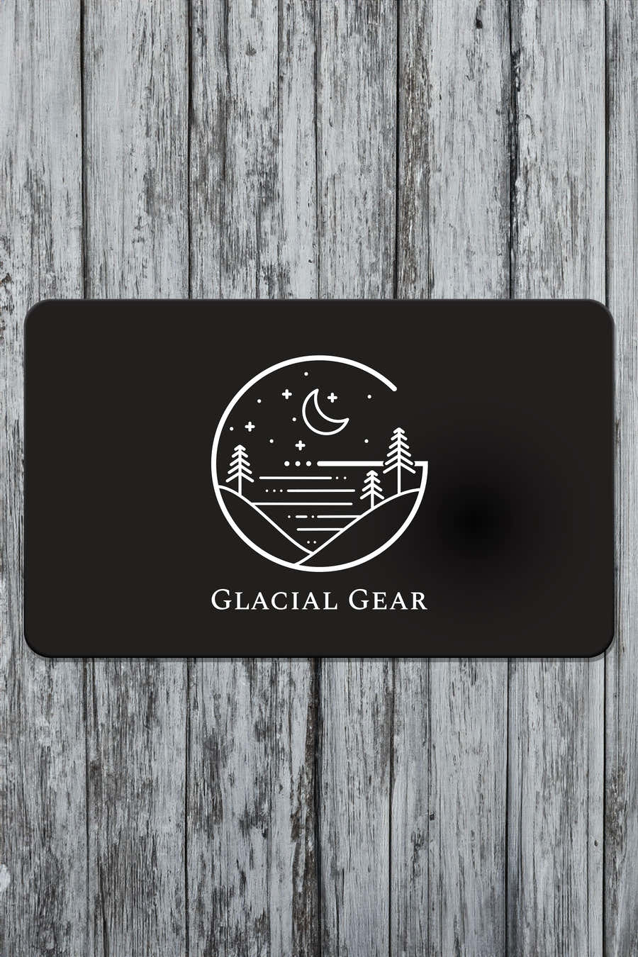 Black Glacial Gear gift card with white hammock, mountain, and moon logo on weathered wood
