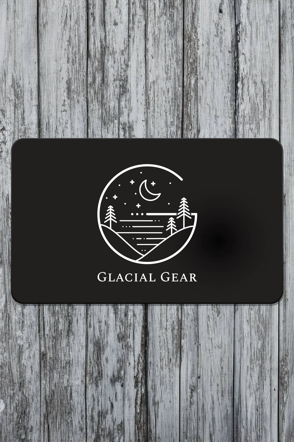 Black Glacial Gear gift card with white hammock, mountain, and moon logo on weathered wood