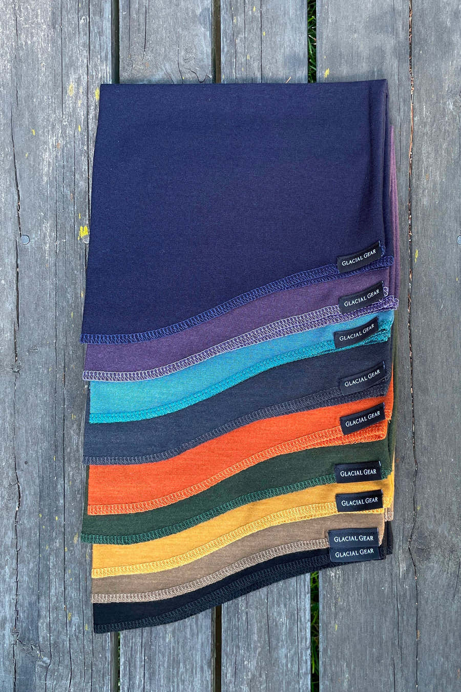 Glacial Gear Merino wool neck gaiters stacked in assorted colors on weathered wood