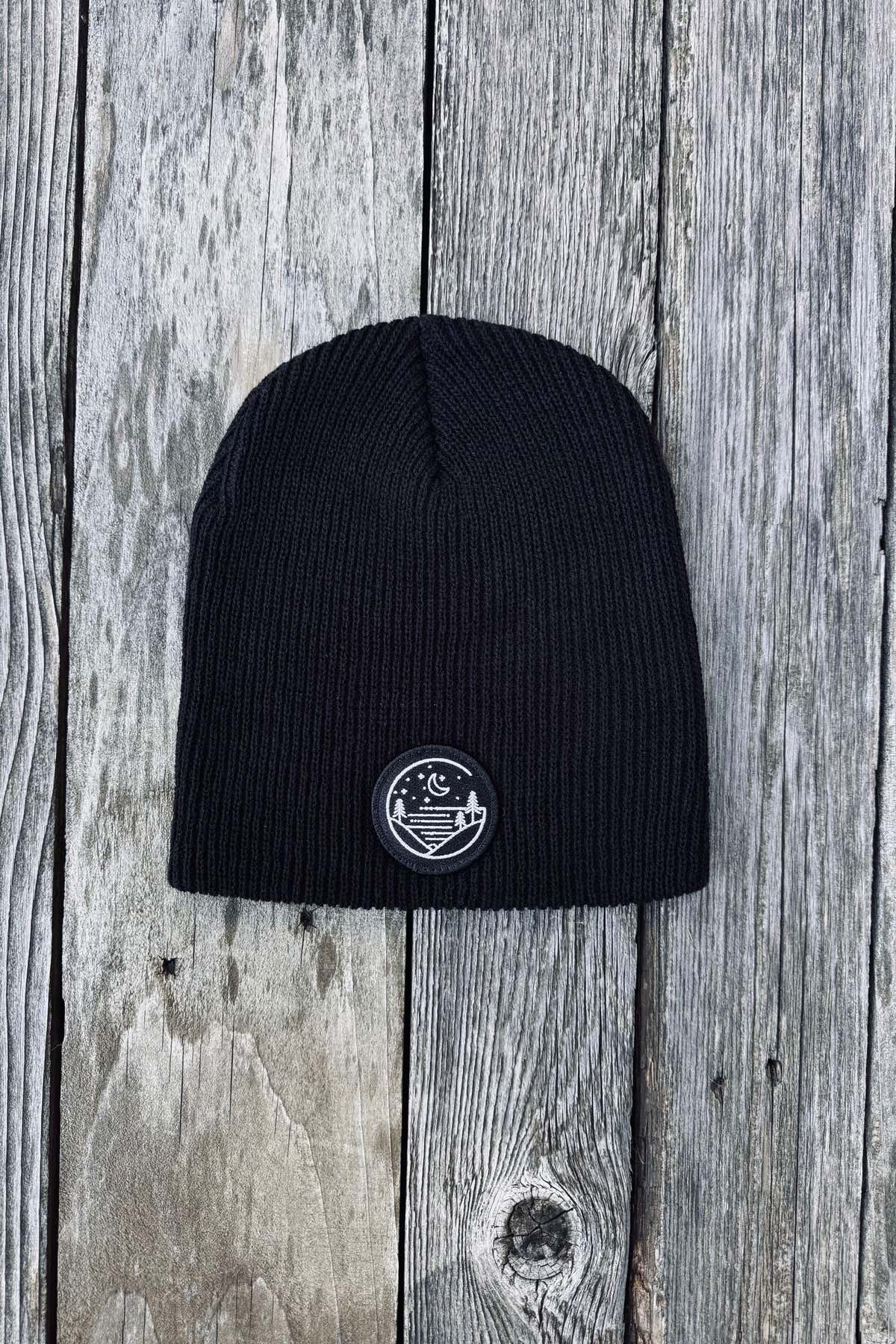 Black rib-knit Glacial Gear beanie with circular logo patch on weathered wood