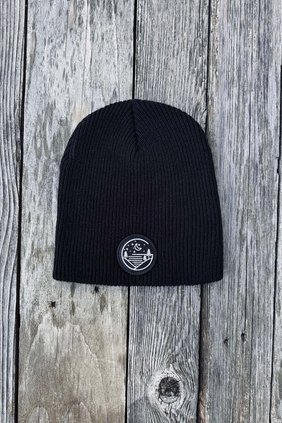 Black rib-knit Glacial Gear beanie with circular logo patch on weathered wood
