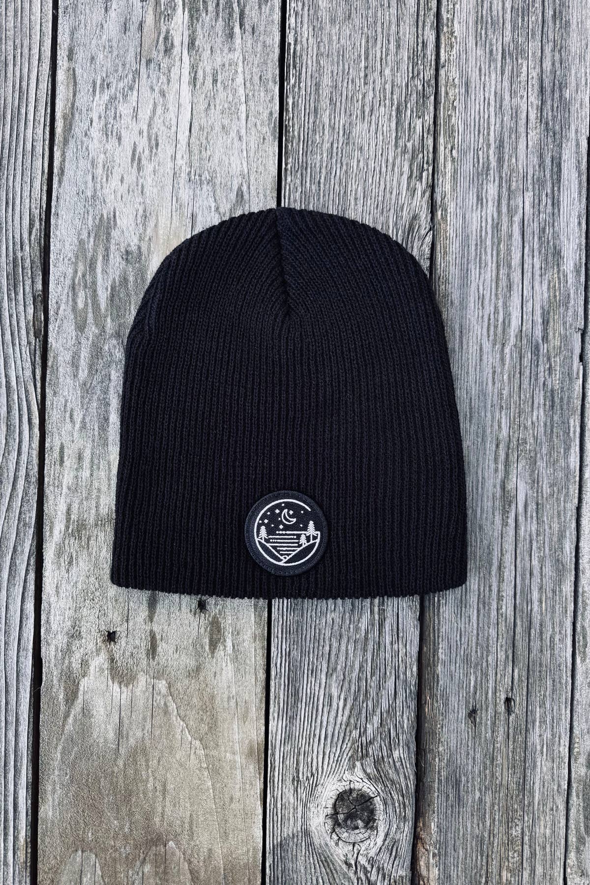 Black rib-knit Glacial Gear beanie with circular logo patch on weathered wood