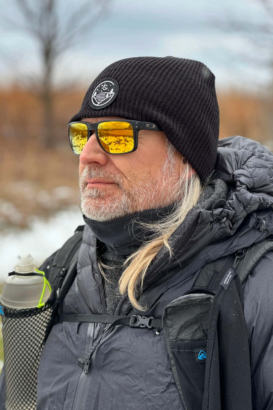 Hiker wearing a black Glacial Gear knit beanie and yellow sunglasses in a snowy setting