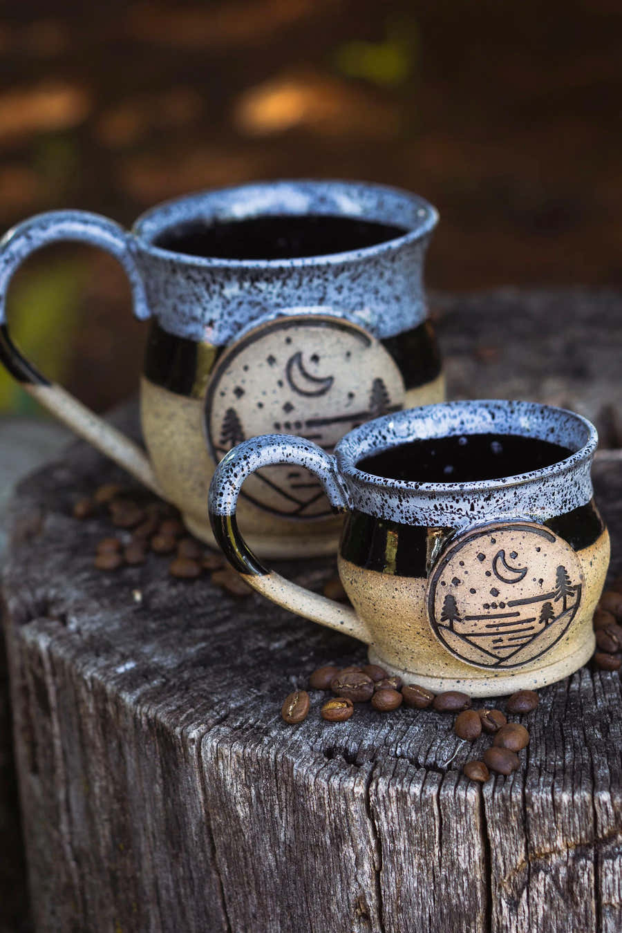 Large and small Glacial Gear ceramic mugs on a tree stump with scattered coffee beans