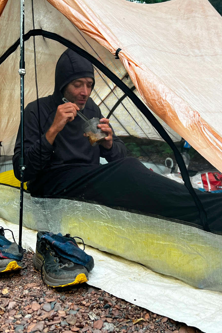 Camper sitting inside a tent with a dark sleeping bag liner covering their legs