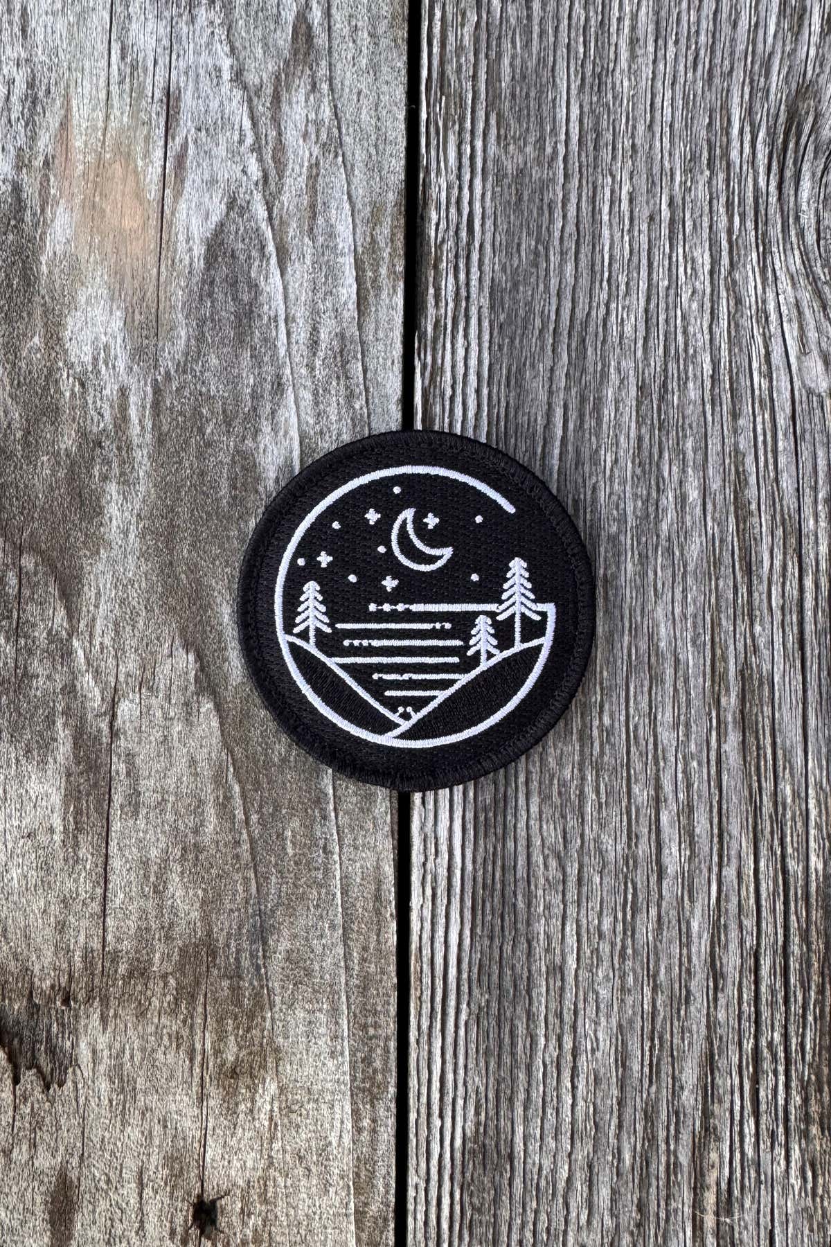 Round black Glacial Gear embroidered logo patch on weathered wood