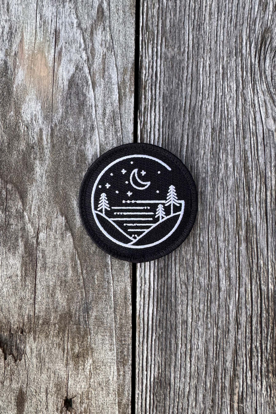 Round black Glacial Gear embroidered logo patch on weathered wood