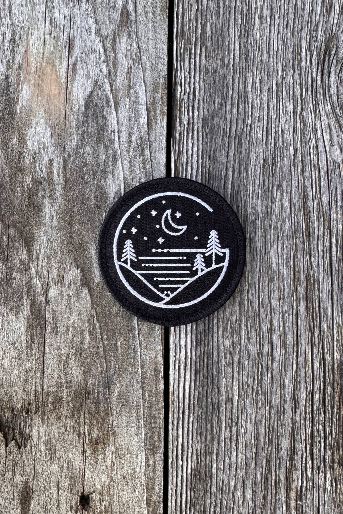 Round black Glacial Gear embroidered logo patch on weathered wood
