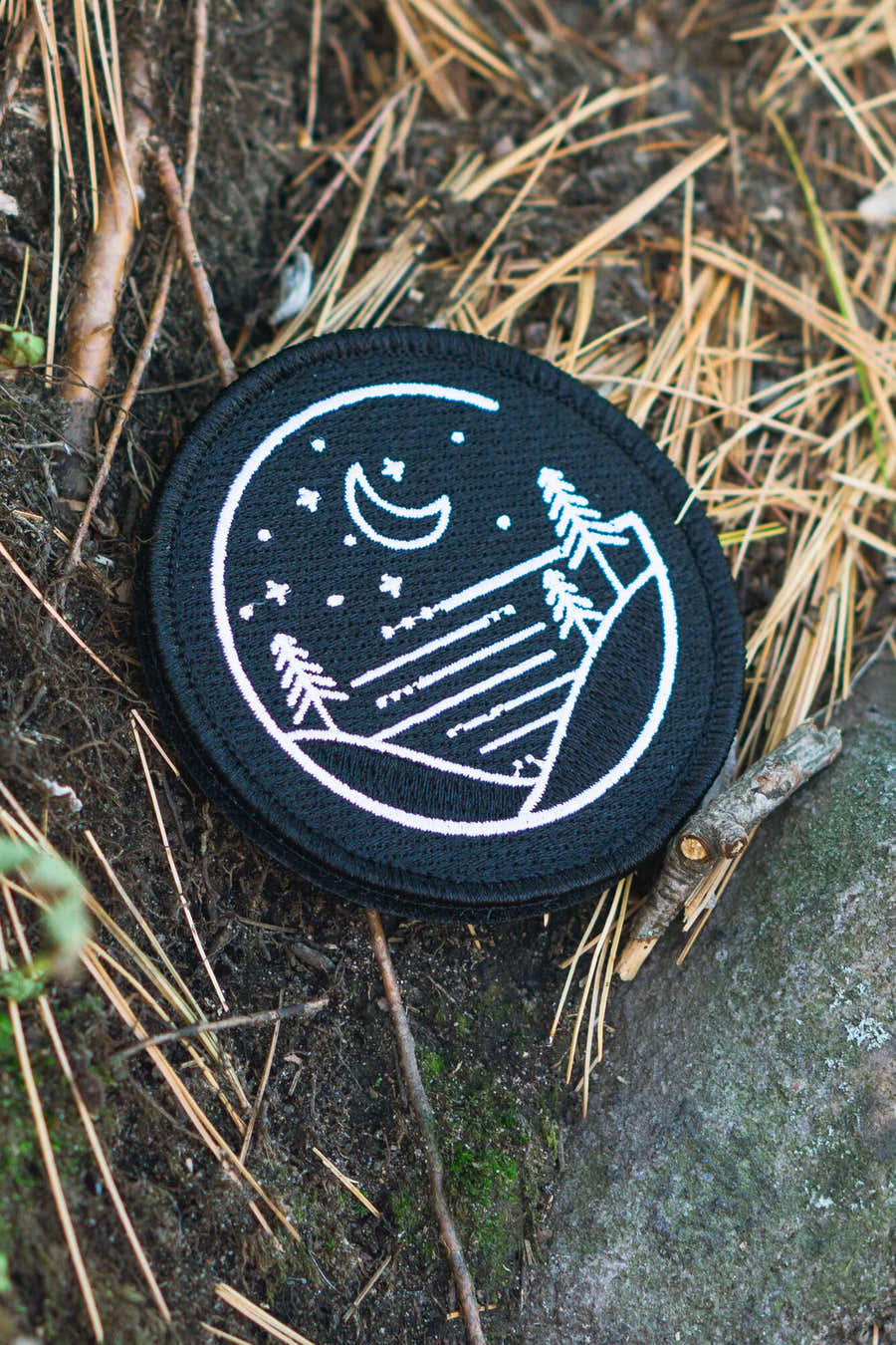 Glacial Gear logo patch resting on pine needles beside a rock