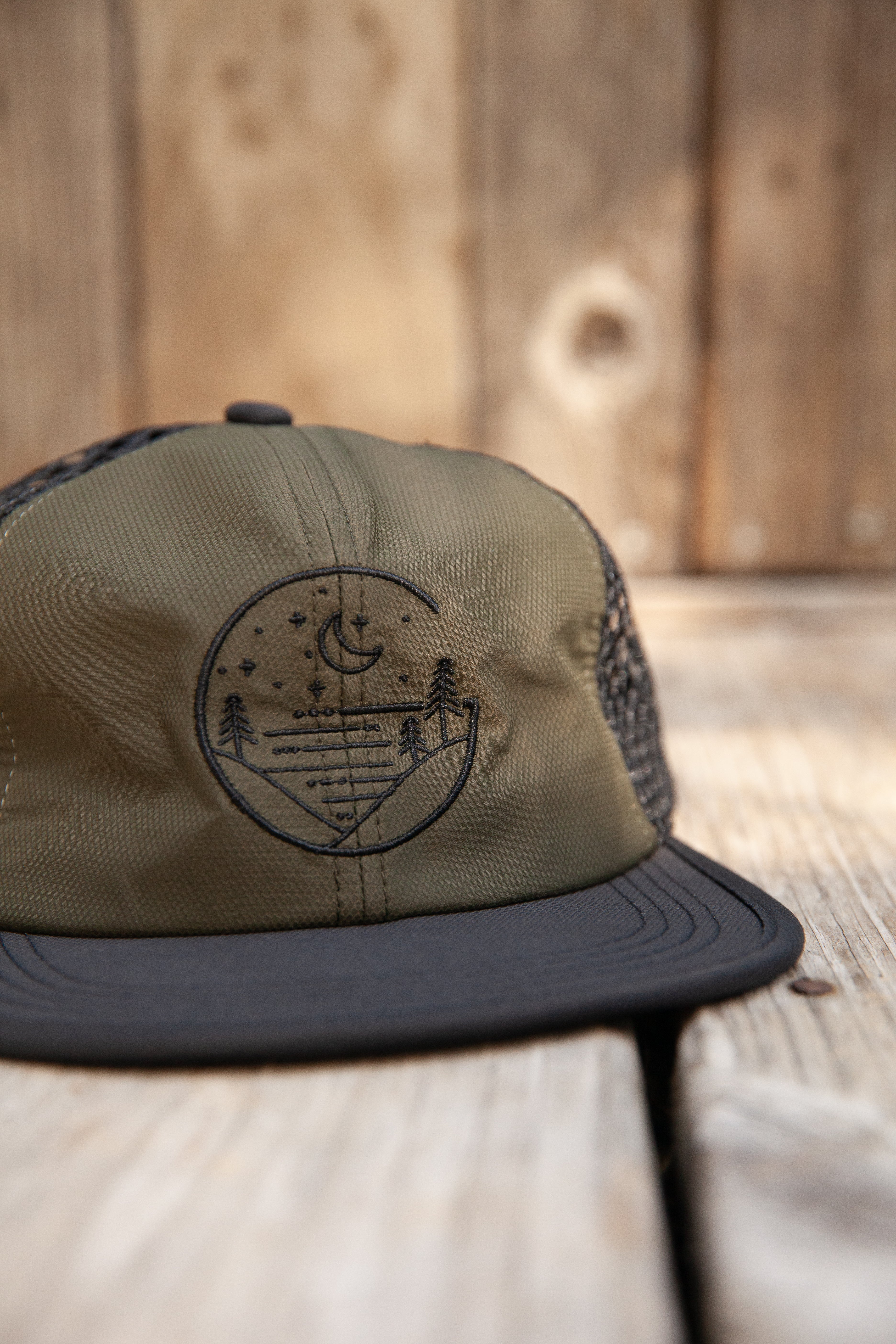 Forest green Glacial Gear Foldable Trail Hat with black brim on weathered wood