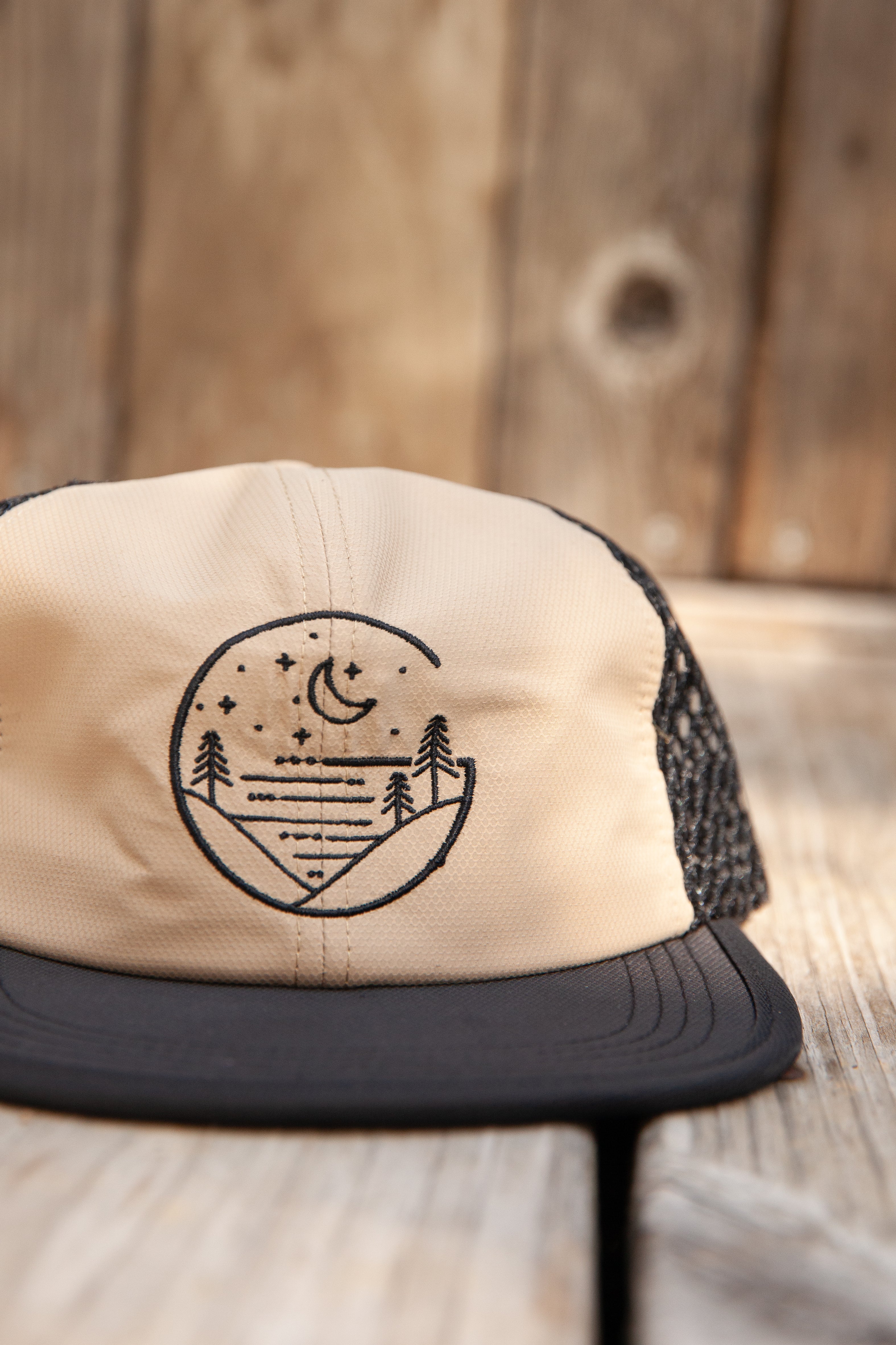 Beige Glacial Gear Foldable Trail Hat with black brim and mesh sides on weathered wood