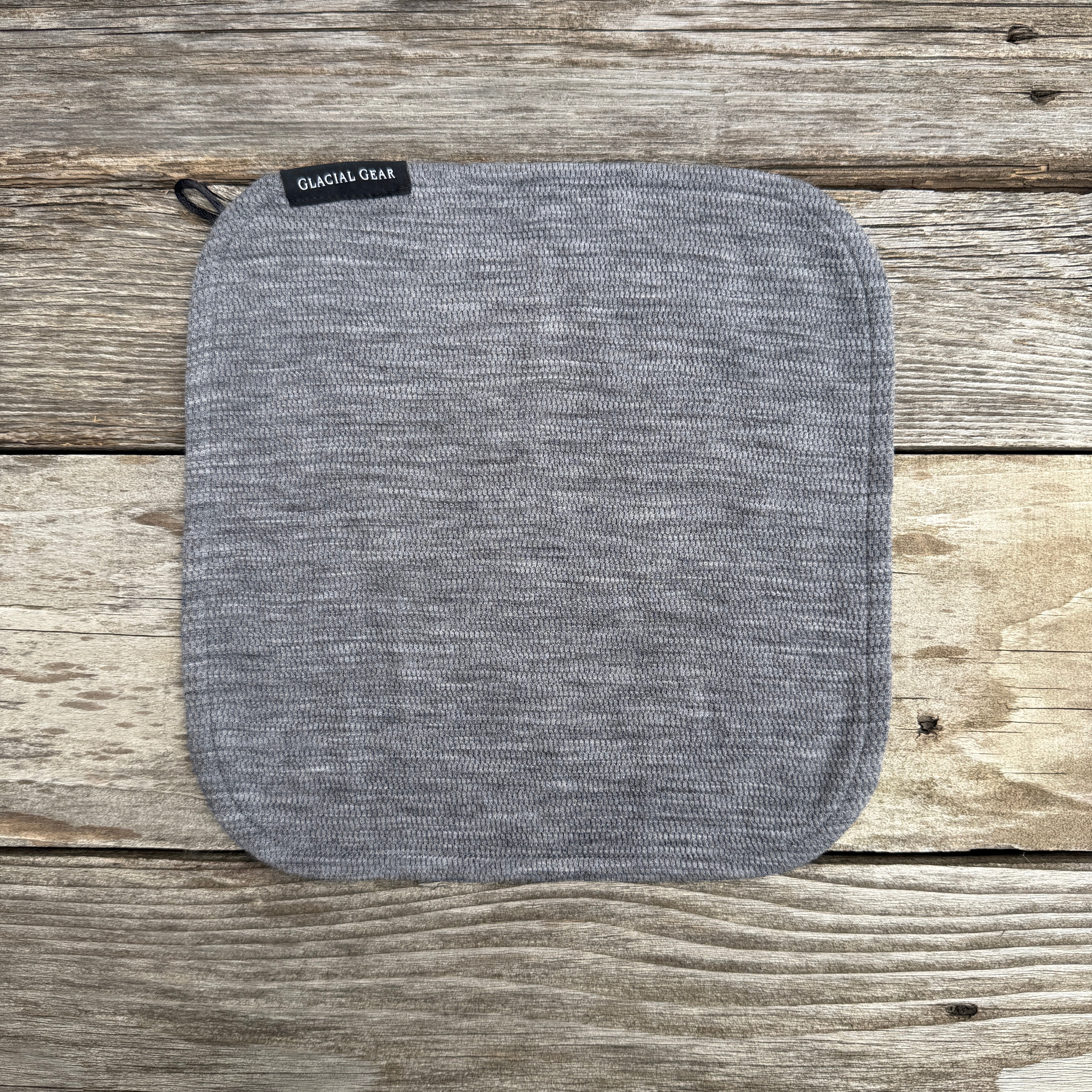 Gray Glacial Gear x Zpacks Trail Rag laid flat with rounded corners on weathered wood
