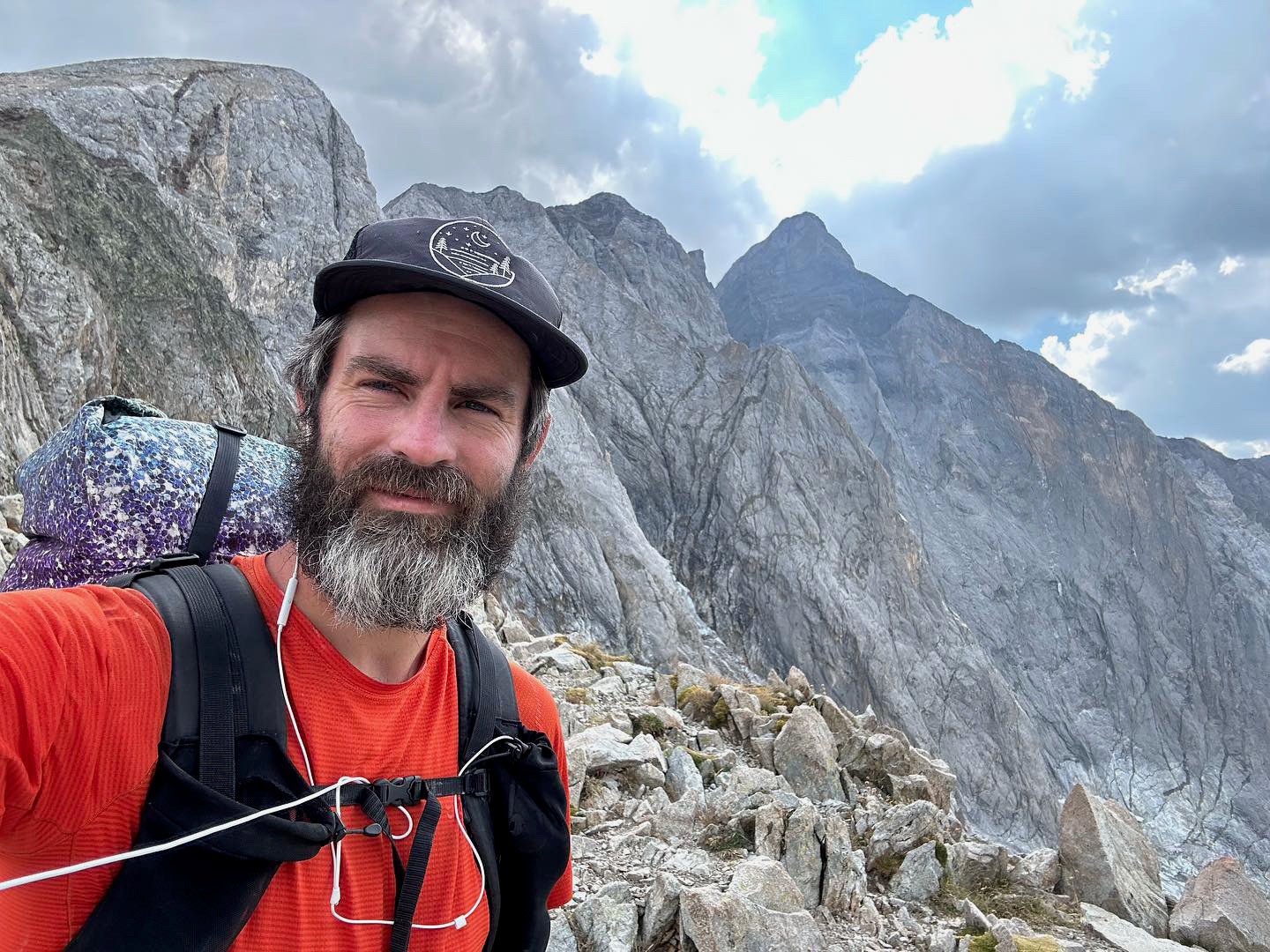 Backpacker in a red shirt wearing a black Glacial Gear Foldable Trail Hat on a rocky mountain ridge.