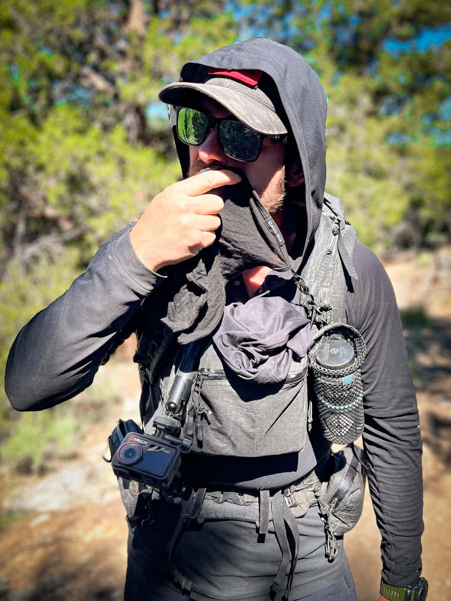 Backpacker wiping his face with a black Merino wool Trail Rag