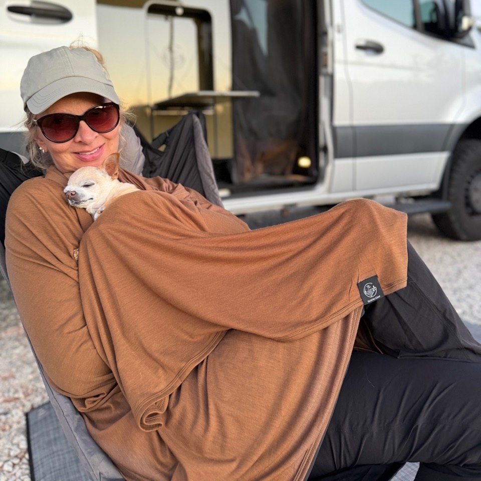 Woman cuddling a sleeping dog in a Bark Merino wool blanket beside a camper van