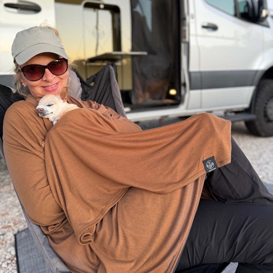 Woman cuddling a sleeping dog in a Bark Merino wool blanket beside a camper van