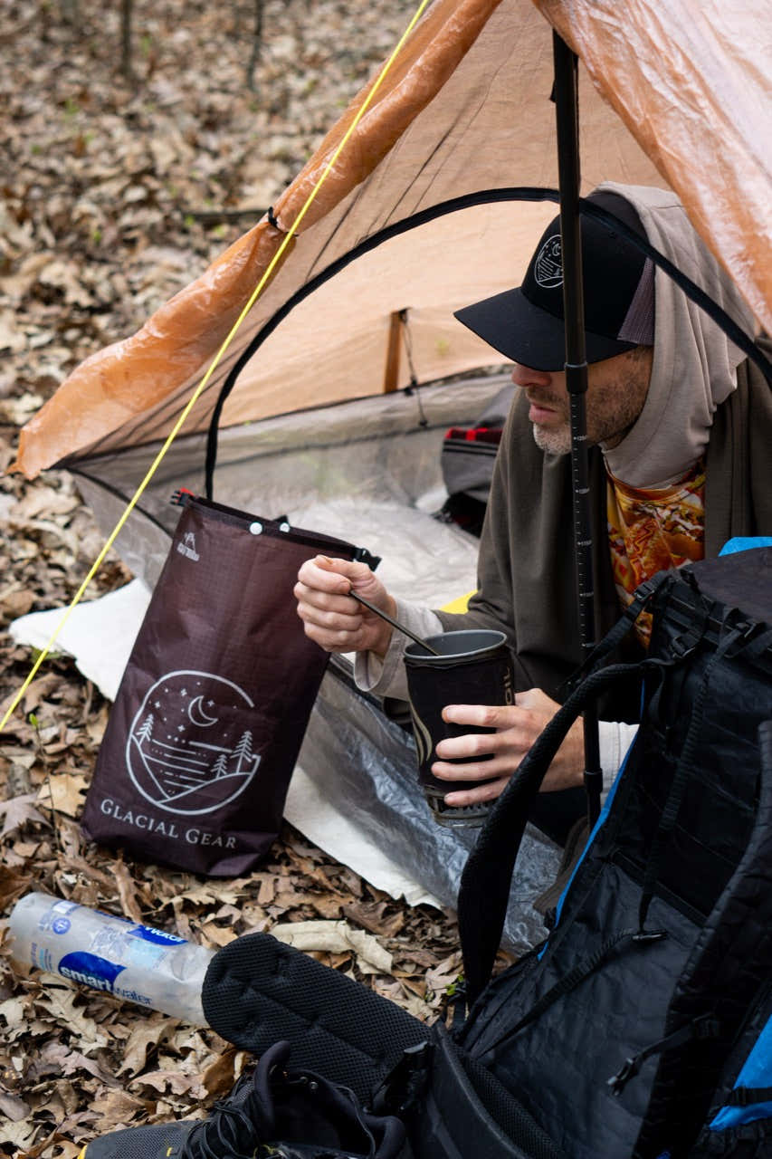 Glacial Gear food bag beside a backpacker preparing a meal under a tent