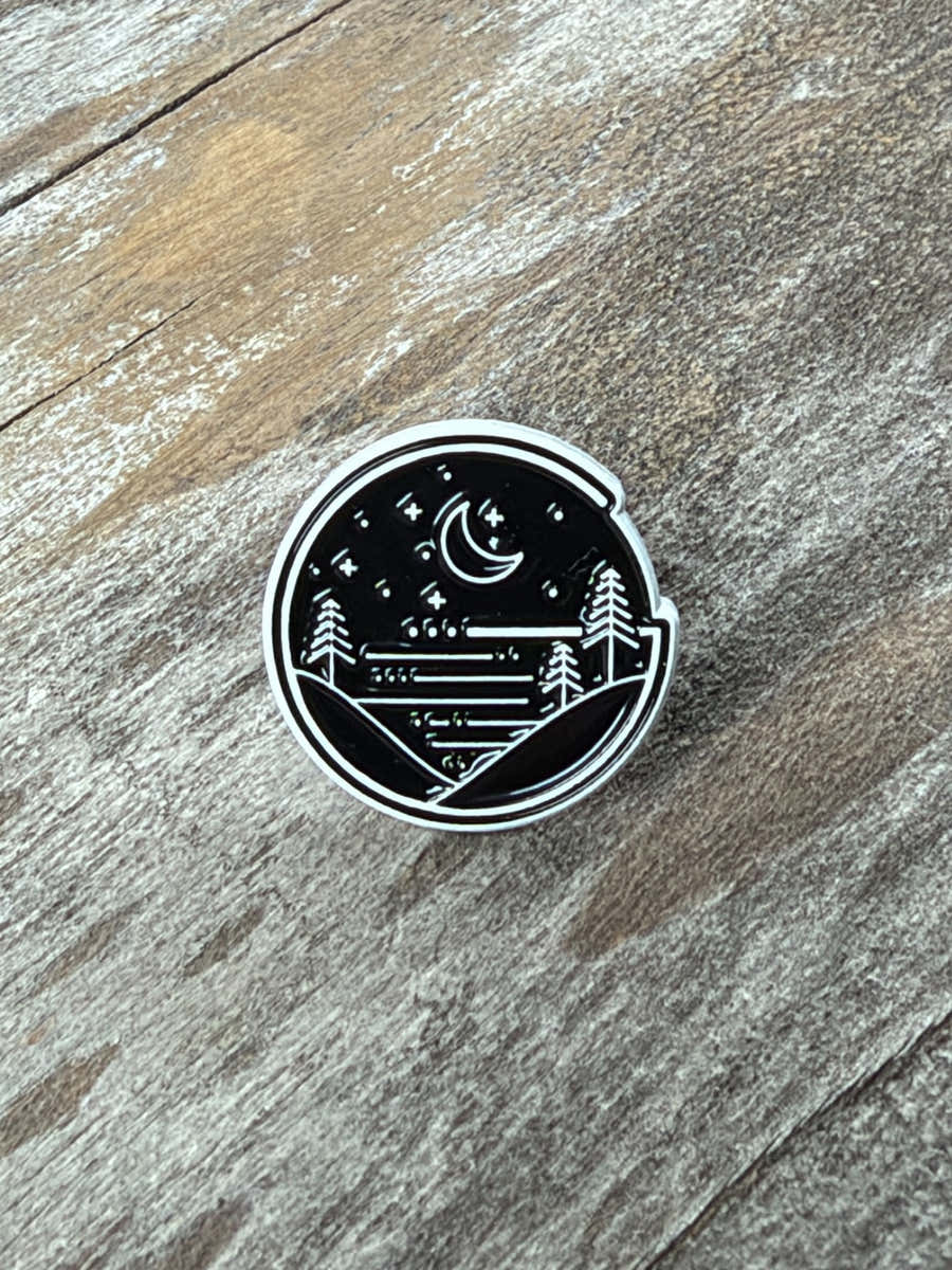 Close-up of the ¾ in Glacial Gear limited edition enamel pin, showing its raised, textured logo on weathered wood