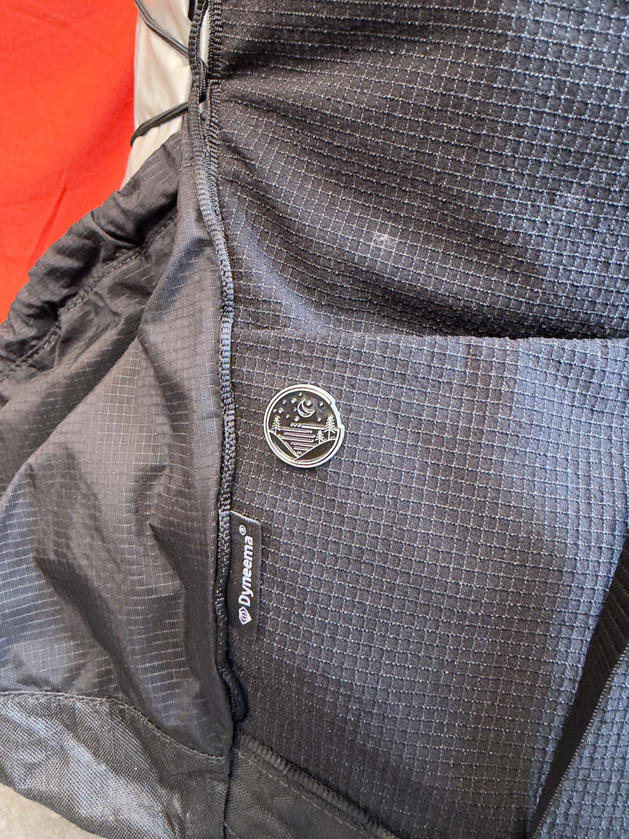 The ¾ in Glacial Gear limited edition enamel pin on a black Dyneema backpack