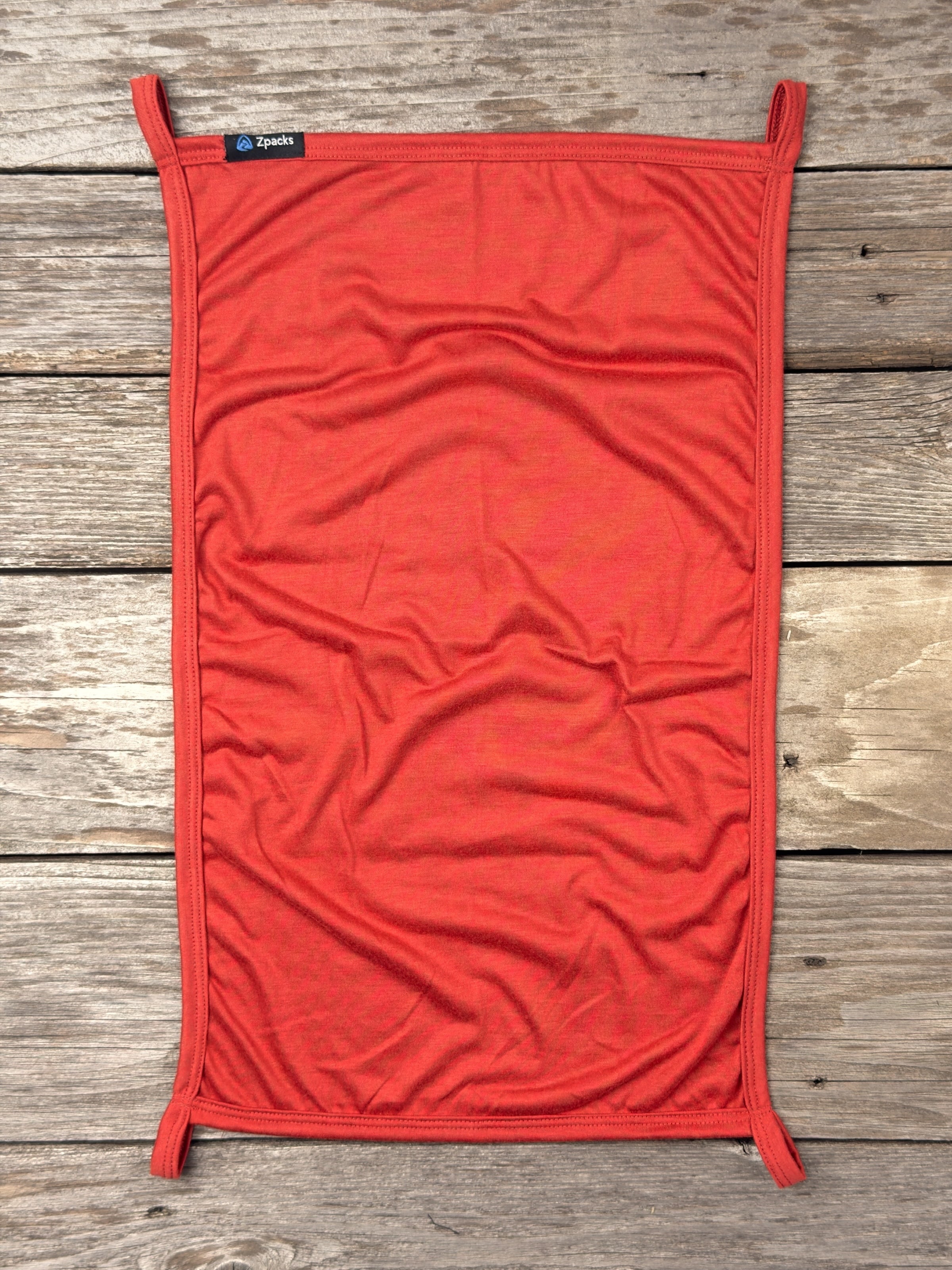 Small Autumn Glacial Gear x Zpacks Camp Towel laid flat on weathered wood, showing its four corner loops