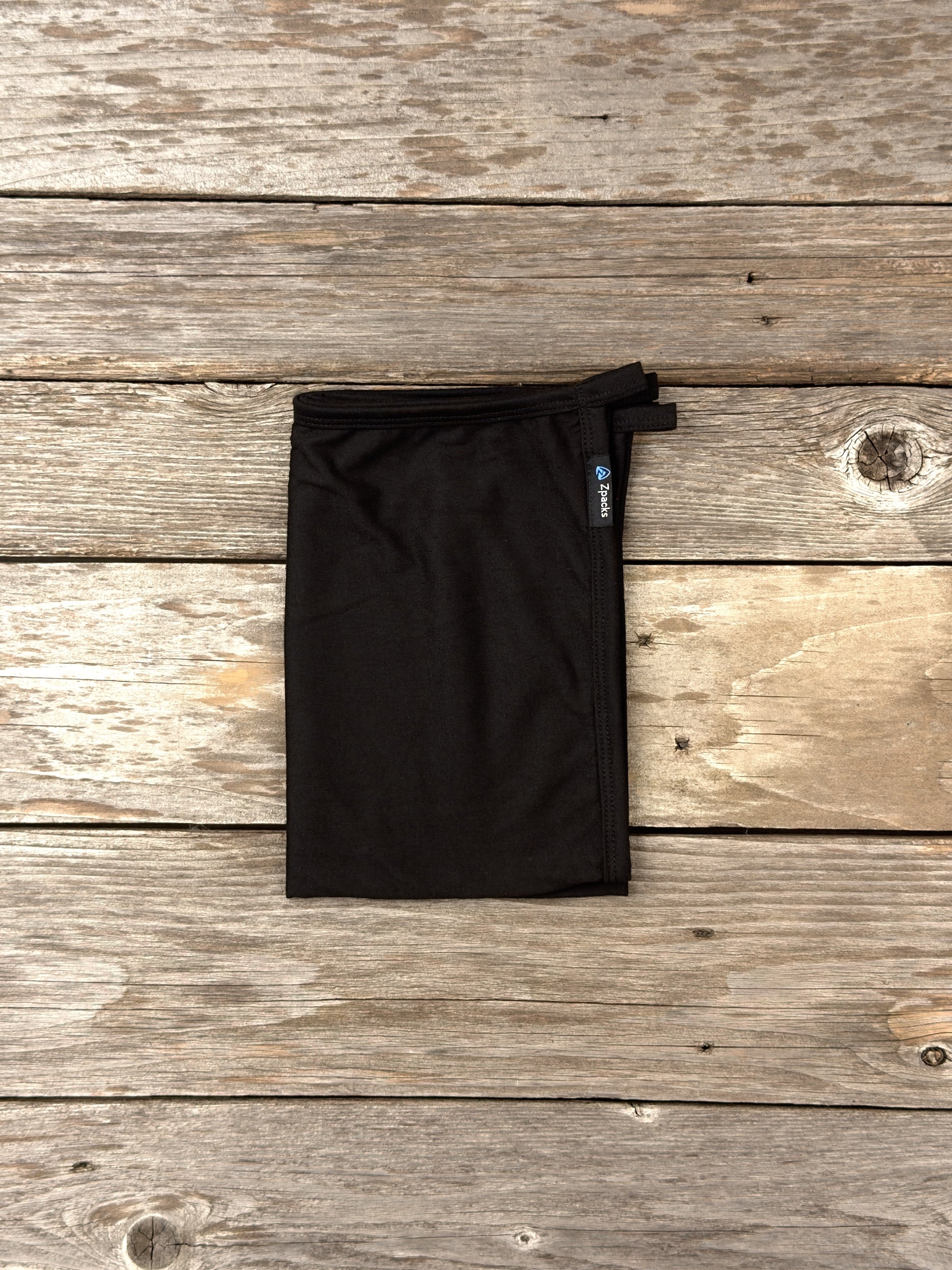 Medium Black Glacial Gear x Zpacks Camp Towel, folded on weathered wood