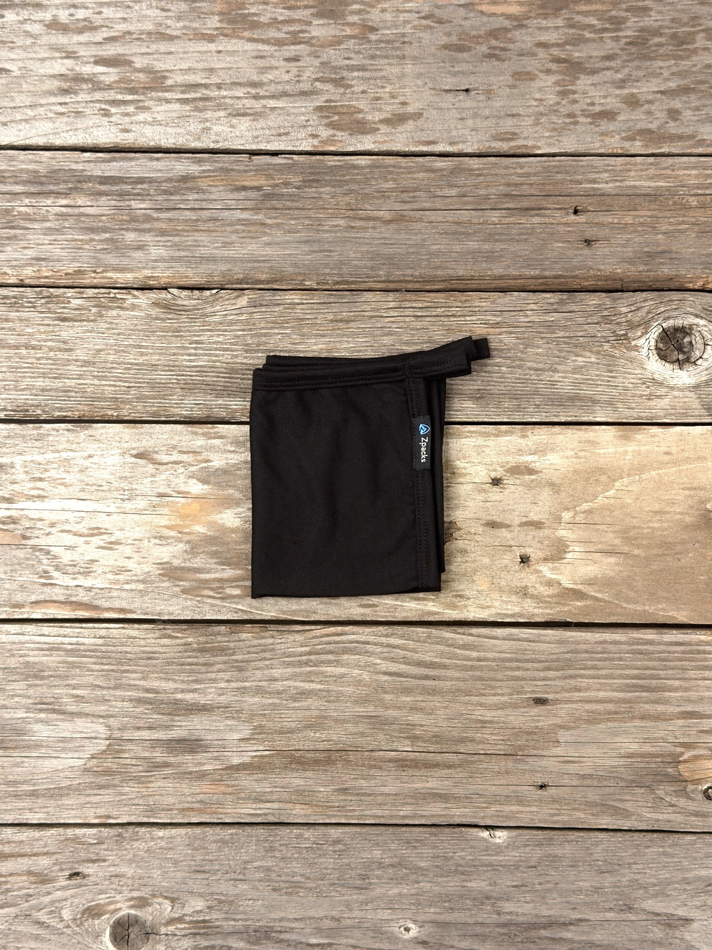 Small Black Glacial Gear x Zpacks Camp Towel, folded on weathered wood