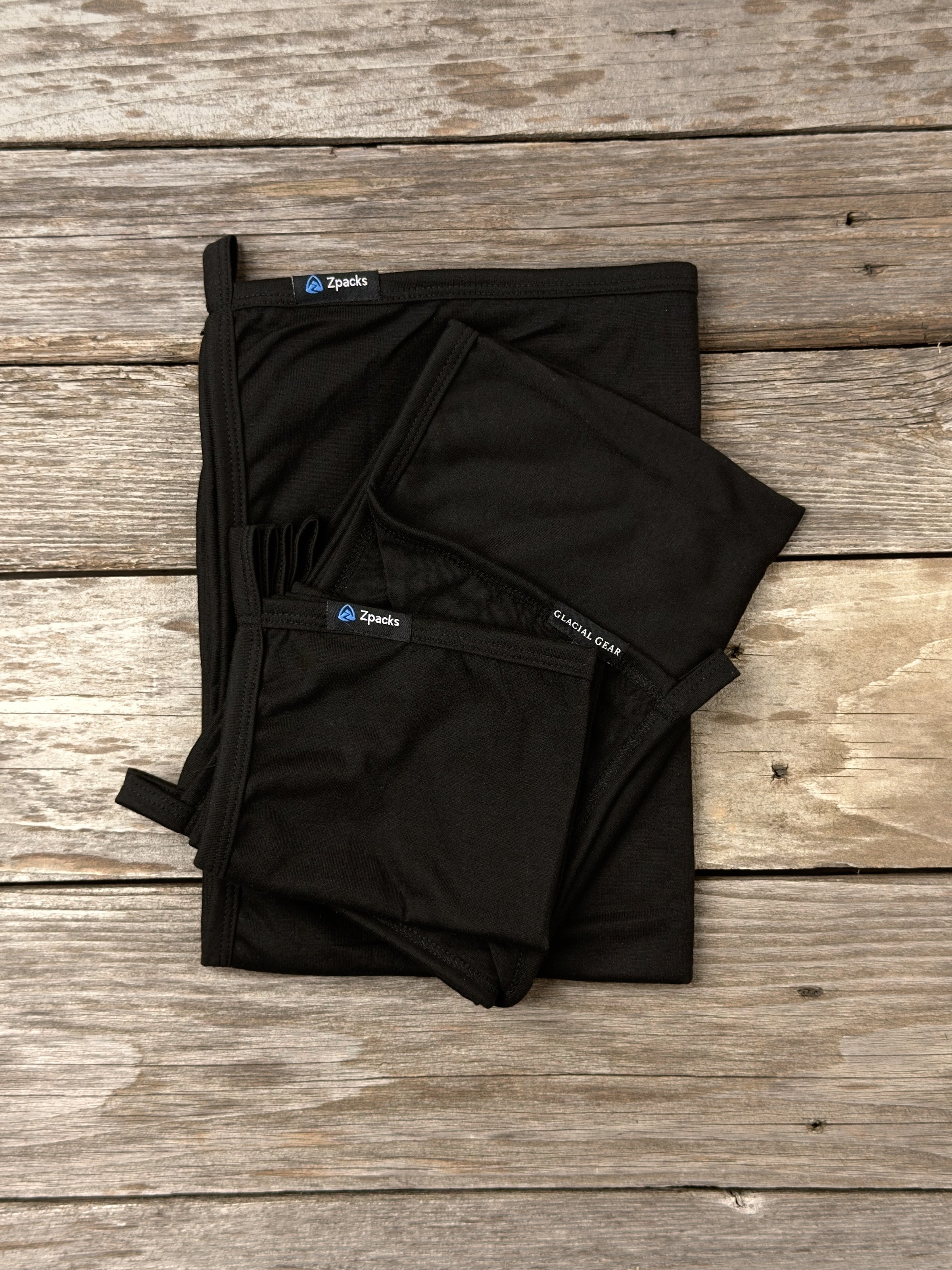 Glacial Gear x Zpacks Camp Towels in Black, folded in Small, Medium and Large on weathered wood