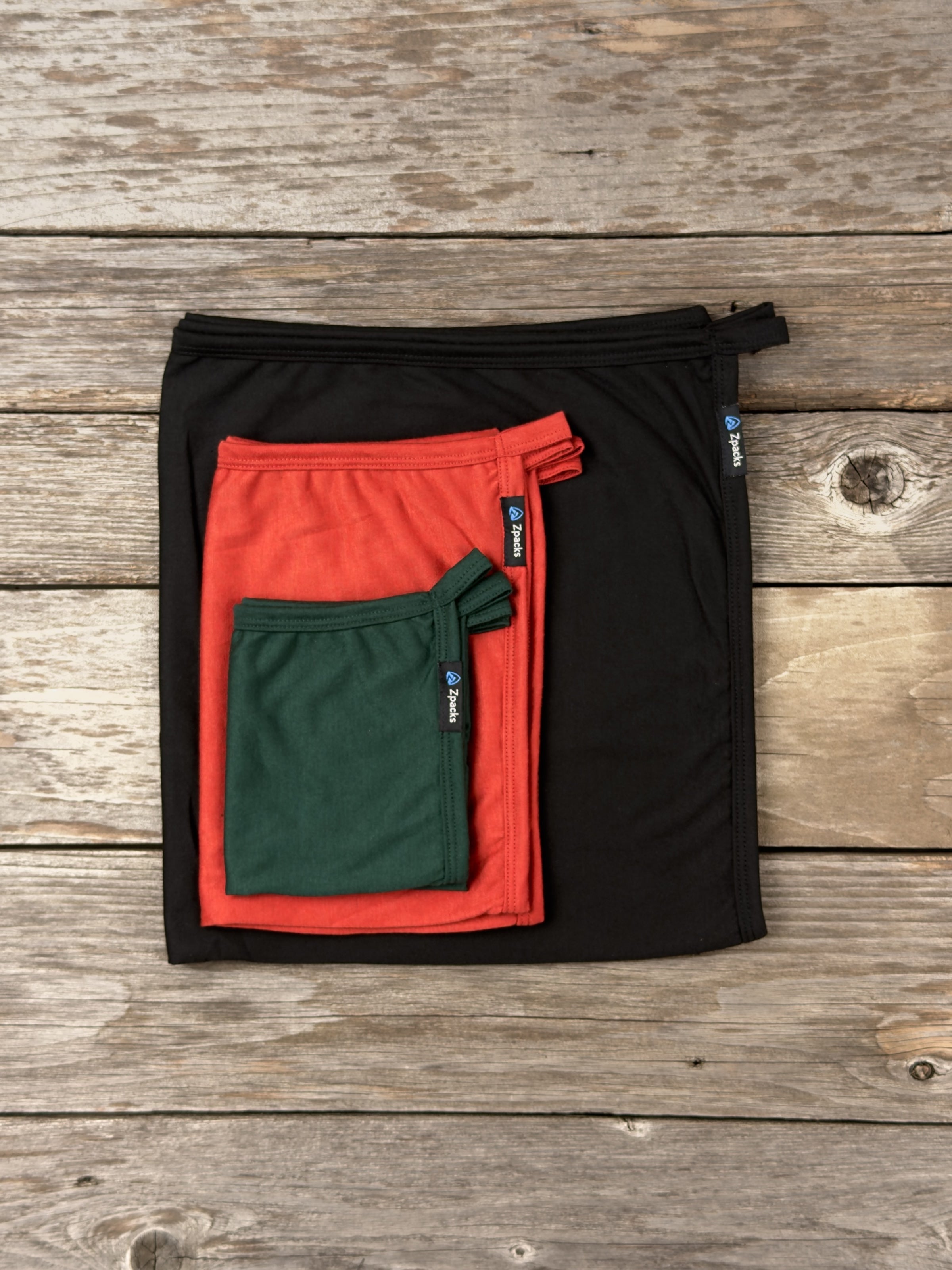 Three Glacial Gear x Zpacks Camp Towel sizes nested together for scale: Large in Black, Medium in Autumn and Small in Forest