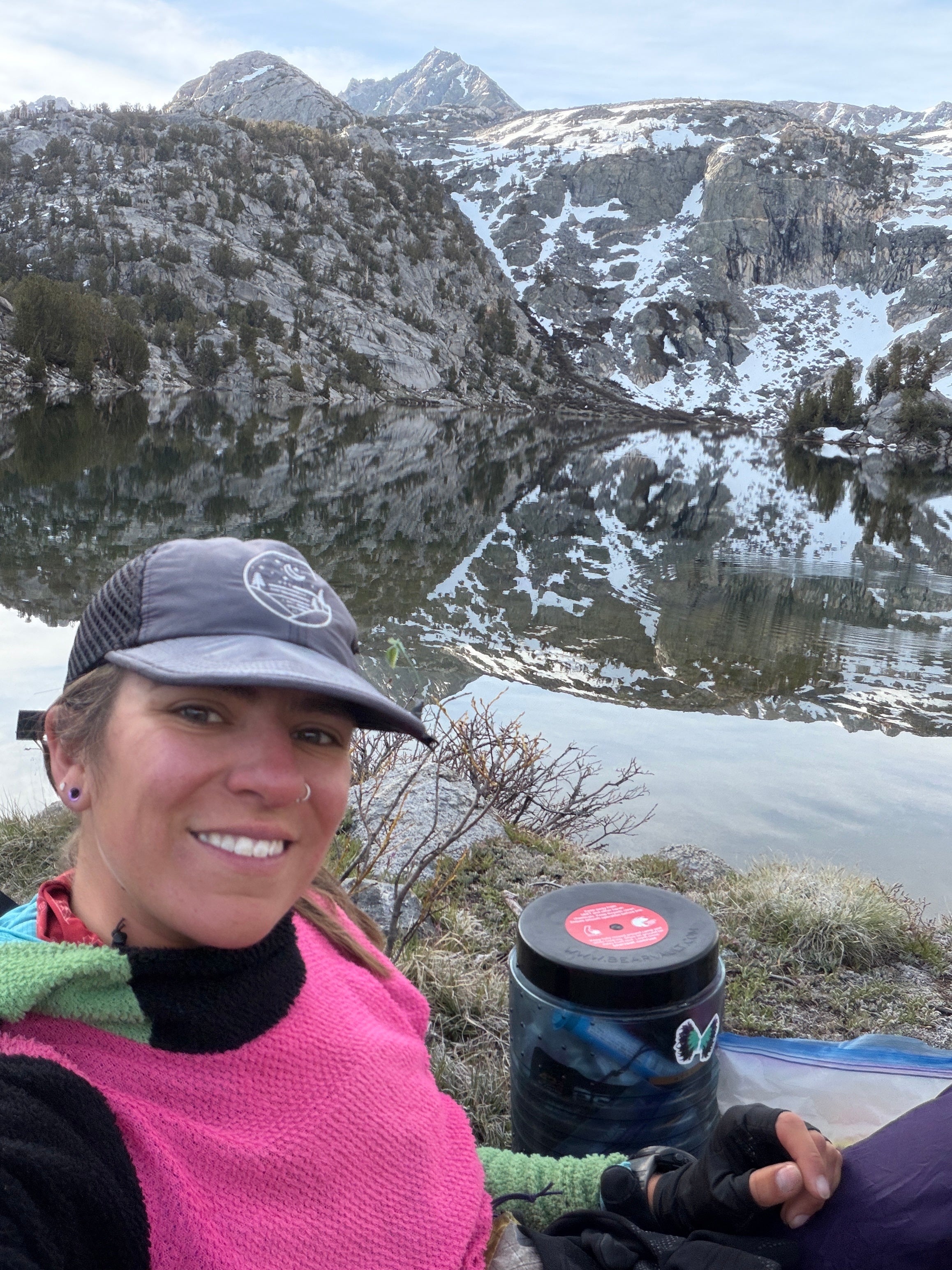 Jocelyn Smith wearing her well-used Glacial Gear Foldable Trail Hat beside an alpine lake