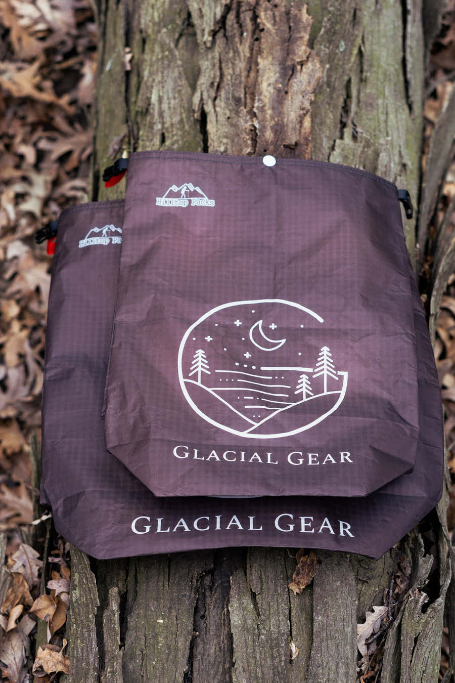 Two Glacial Gear ECOPAK food bags in different sizes hanging against a tree