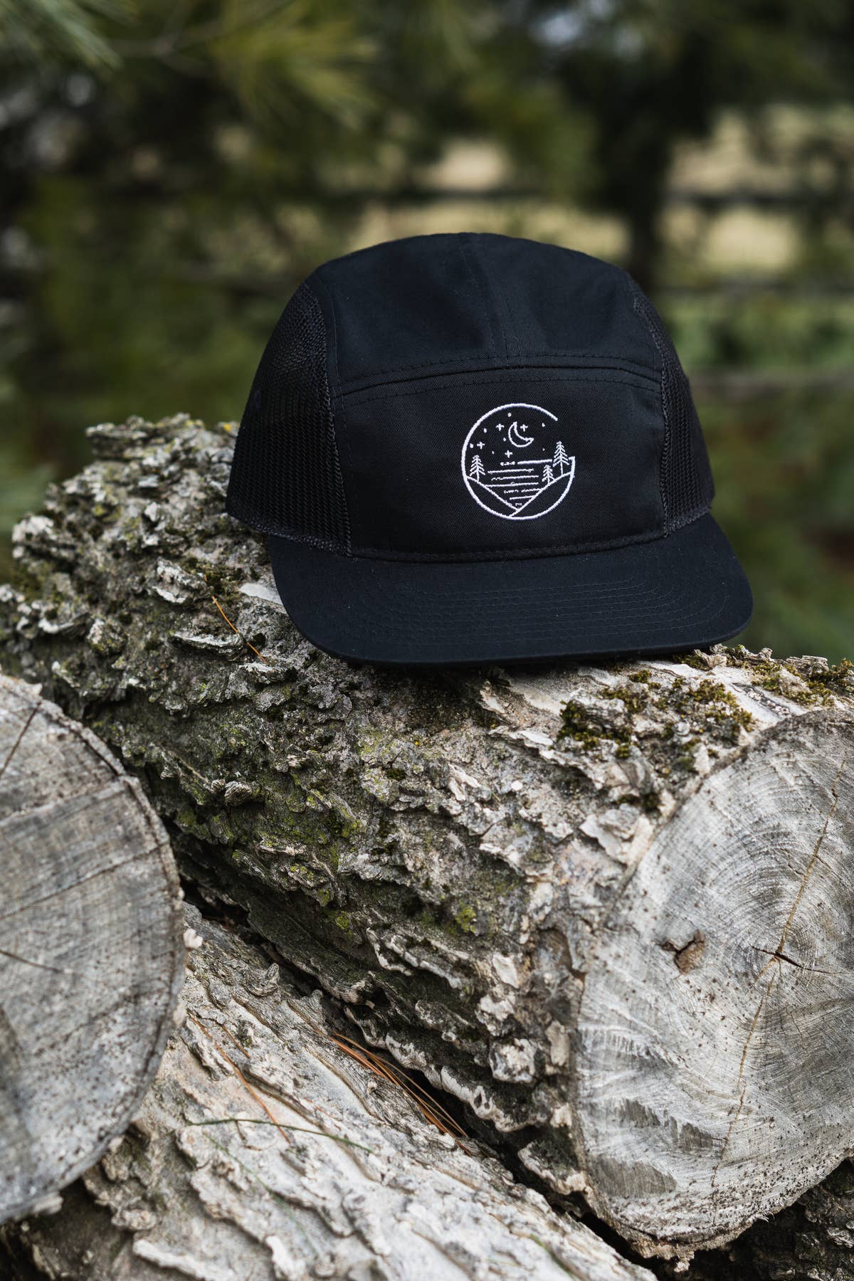 Black Glacial Gear cotton twill five-panel hat with mesh sides and embroidered logo on a mossy log