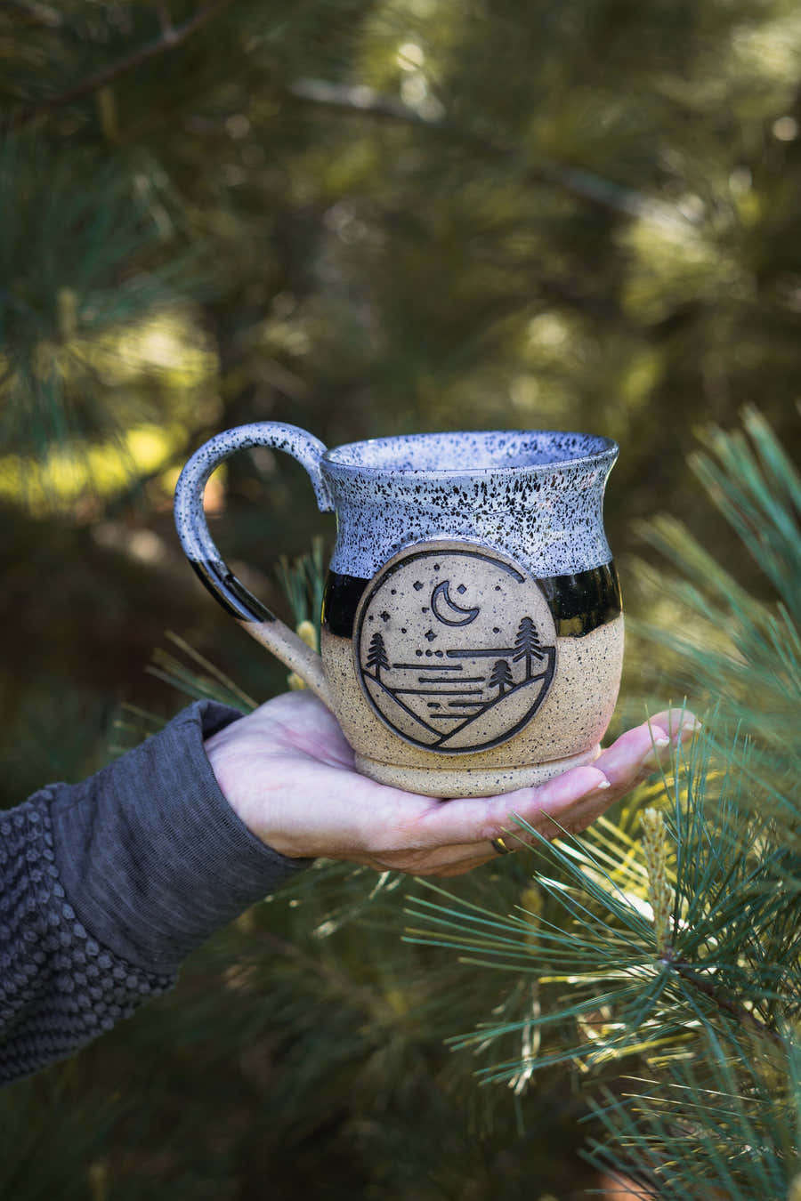Hand holding a large Glacial Gear ceramic mug with a blue rim and logo outdoors