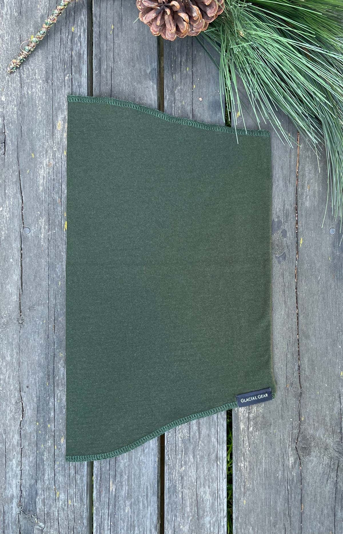 Cache-cou Glacial Gaiter vert en laine mérinos posé à plat sur du bois patiné
