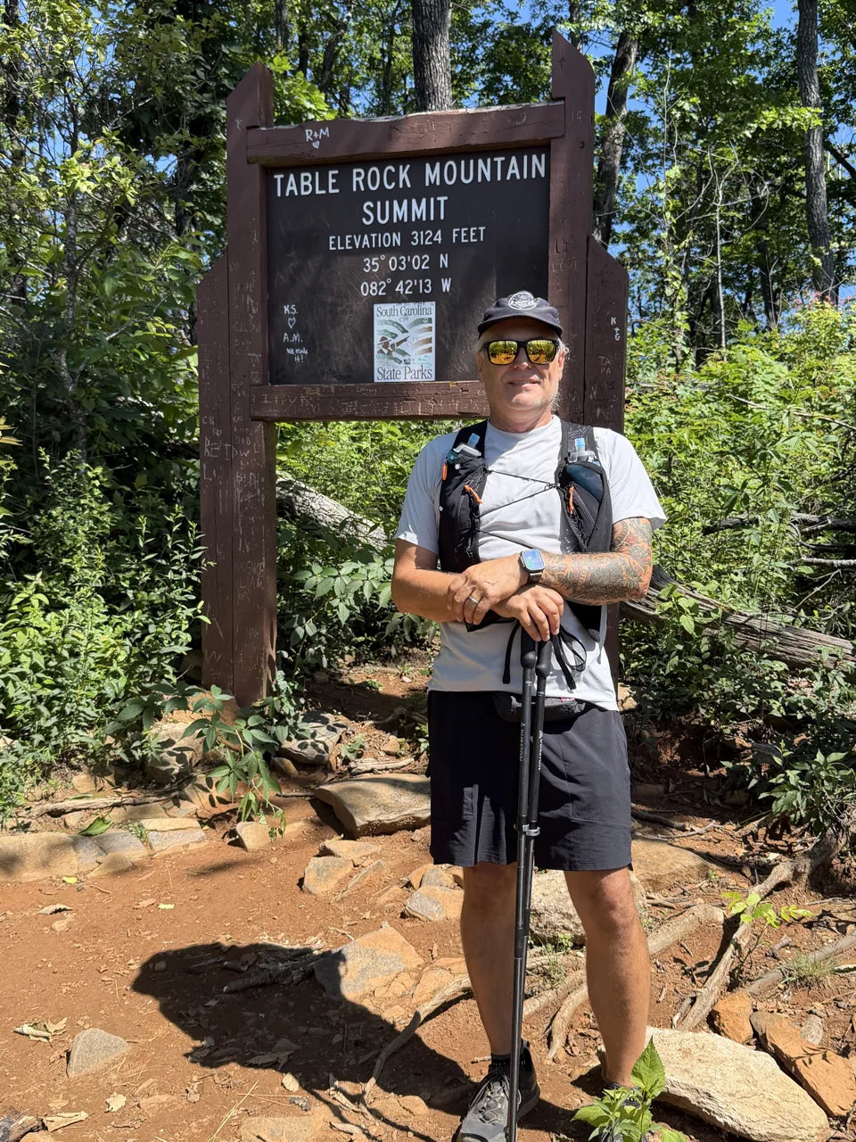 Hiker beside the Table Rock Mountain summit sign, surrounded by forest.